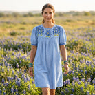 Sky blue chambray Halftime Dress with bluebonnet embroidery on the yoke and embroidered puff-sleeve cuffs, worn in a bluebonnet field