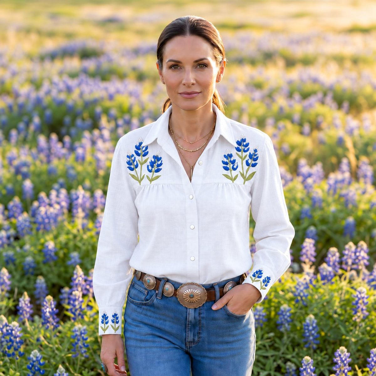White denim pearl-snap Cowgirl+ Blouse with blue bluebonnet embroidery on the yoke and cuffs, tucked into jeans with a concho belt