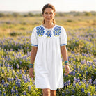 White denim Halftime Dress with blue bluebonnet embroidery on the yoke and embroidered puff-sleeve cuffs, worn in a bluebonnet field
